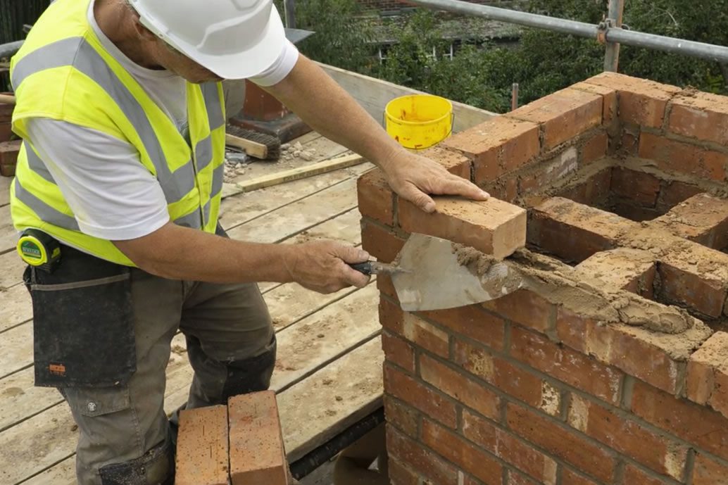 tradesman roofer rebuilding chimney stack with red brick